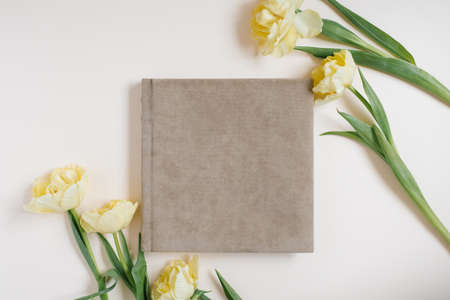 Composition with a wedding or family photo album, a bouquet of flowers of yellow tulips on a light background. Flat lay, top view still life.の写真素材