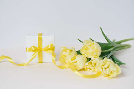 Spring composition of a bouquet of yellow tulips, a gift with a yellow bow and ribbon on a white background. The beginning of spring, women's day, mother's day, birthday. front viewの写真素材