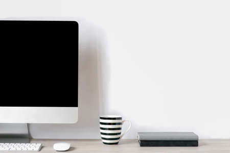 Technologies and concept of remote work. Front view of handsome copywriter workplace with computer, cup and notepads on tableの写真素材