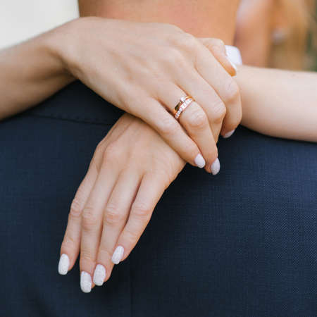 The bride hugs the groom by the neck. Close-up of her hands with an engagement ringの写真素材