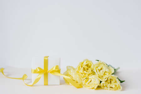 Colorful bouquet of yellow tulips and gift box in front of white wall with place for your congratulationsの写真素材