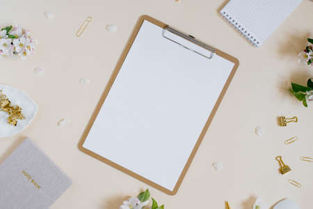 Blank sheet of paper notepad with a clip, apple tree branches with flowers, notepads and paper clips on a beige background. A minimal home office desktop. Flat lay, top view.の写真素材