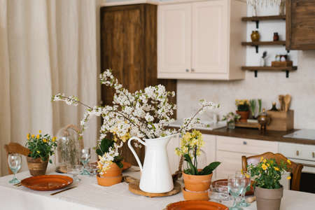 A bouquet of spring white flowers on branches in a vase on the kitchen table. Scandinavian style of...