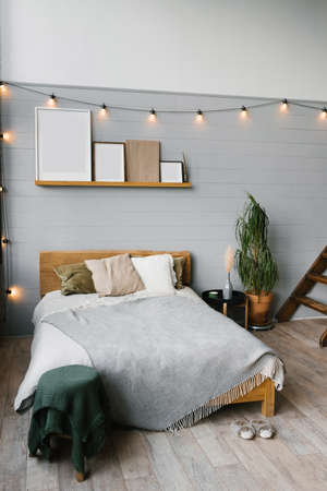 Bedroom interior Scandinavian style. A bed with pillows and a blanket, a moccap of paintings on the shelf above the bed, a potted houseplantの写真素材
