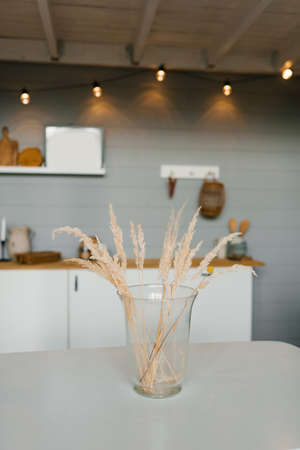 Dry grass branches in a glass vase on the table in the Scandinavian kitchen