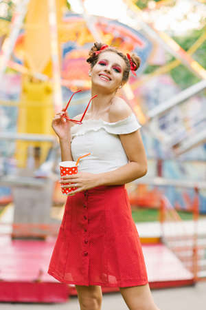 A beautiful young woman walks in an amusement park and holds a paper cup in her handsの写真素材