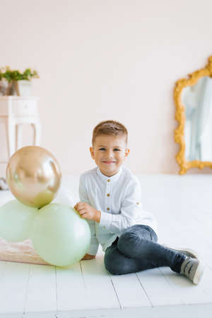 A child boy is sitting on the floor and holding balloons in his hand at home and smilingの写真素材