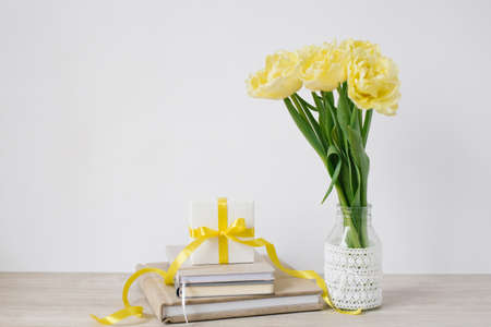 A lot of notepads in a stack, a bouquet of yellow spring tulips and a gift box on the desktop of a freelancer or blogger woman. Women's day, valentine's day or birthday. front viewsの写真素材