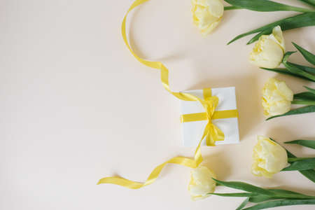 Gift with a bow and a bouquet of spring yellow flowers tulips on a light background with copy spaceの写真素材