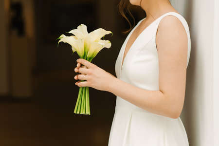 Delicate white bouquet of calla lilies in the hands of the bride at the weddingの写真素材