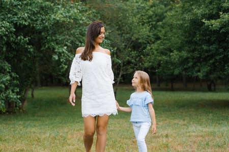 A little daughter holds her mother's hand. Mother and daughter walk in the Park in the summer and look at each otherの写真素材