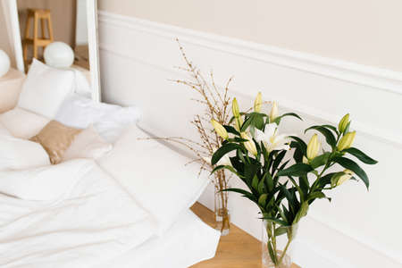 White lily flowers in a vase, tree branches in a vase near the bed. Details of the interior decor of the houseの写真素材