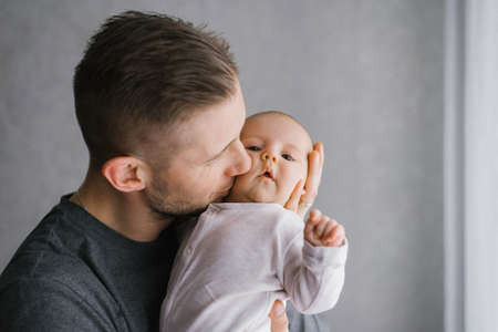 Dad holds his baby in his arms at home and kisses the baby on the cheekの写真素材