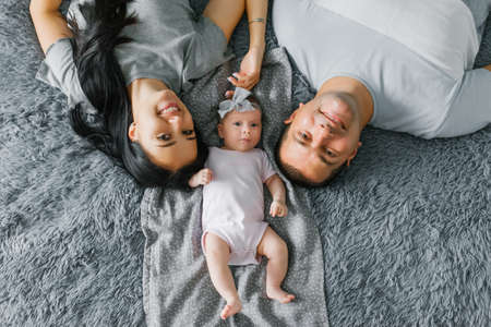 A happy young family with a baby are lying on the bed and smiling. top view