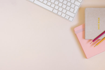 Office desk, notebooks, keyboard and colored pencils on a beige background. Minimal business concept...