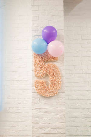 Pink number 5 and balloons are hanging on a white brick wall. The decor of the children's room for the child's birthdayの写真素材