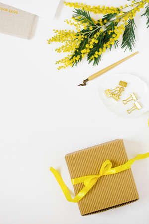 Yellow mimosa flower, gift box with bow stationery and pen for calligraphy with notebooks on white background with copy space, flat layの写真素材