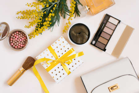 Flat lay fashion blogger. Decorative cosmetics and perfume, eye patches, women's handbag and a branch of yellow mimosa flowers on a white backgroundの写真素材