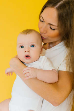 Caring mother holds her baby son in her arms and kisses himの写真素材