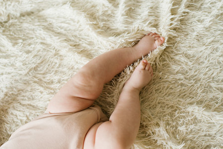 Belly and legs of a newborn baby in a bodysuit lying on a light bed, top viewの写真素材