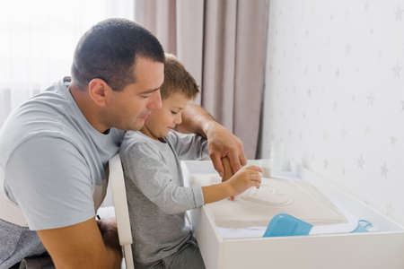 Dad and his baby son play at home with quartz sand