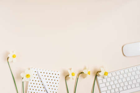 Workplace with a diary, pen, keyboard, mouse and daffodil flowers on a light background. Top view,...