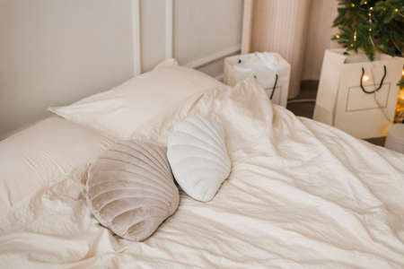 Pillows in the form of seashells lie on a light bed in the bedroom, decorated for Christmasの写真素材