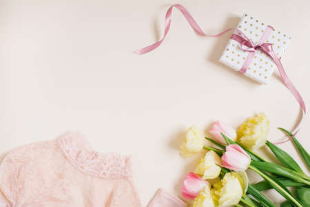 Women's clothing, gift box and tulip flowers. Minimalistic composition in pastel beige and pink...