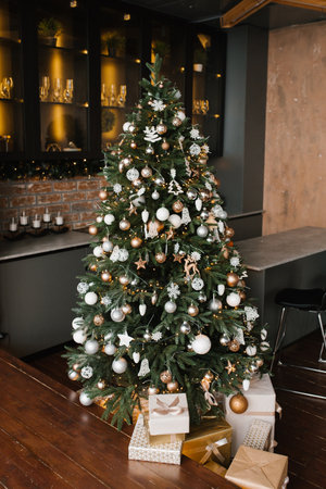 Decorated gold and silver Christmas tree with gifts under it for the new year in the loft-style...