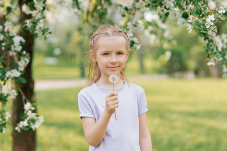 Girl holds a dandelion in her hands in the park in springの写真素材