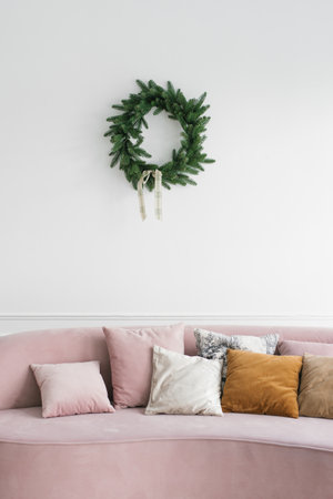 Bright cozy living room with a pink sofa, over which hangs a Christmas wreathの写真素材