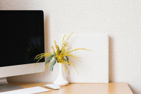 Home office with a computer, a bouquet of mimosa flowers in a vase.