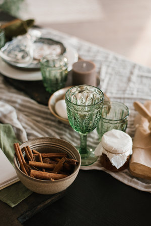Festive Christmas table setting. Green glass glasses and cinnamon sticks in a clay plate on the tableの写真素材