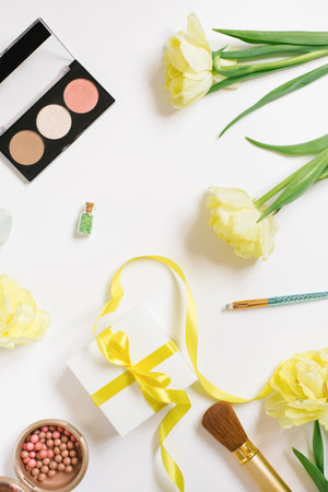 Makeup products with yellow tulip flowers and a gift box with a bow on a white backgroundの写真素材