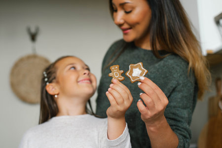 Smiling mom and her daughter are holding Christmas cookies in their kitchenの写真素材