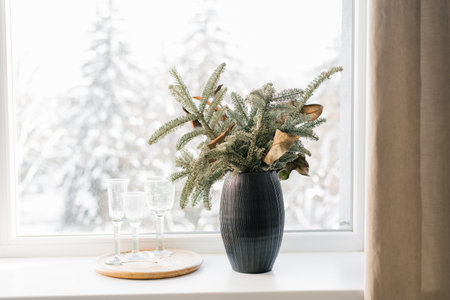 Christmas composition of Christmas tree branches in a black vase on the window of a cozy house
