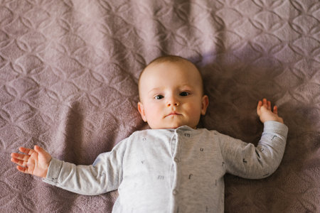 Portrait of a cute charming smiling white Caucasian boy of six months old lying on a bed and looking...