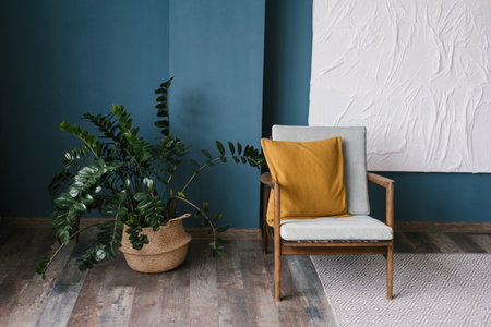 Vintage armchair with a yellow cushion against a blue wall in the living room. Indoor plant...