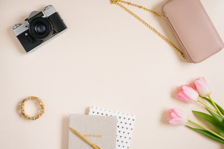 Notebooks and a bouquet of pink tulip flowers, a bag, a camera. Workplace of a female travel...