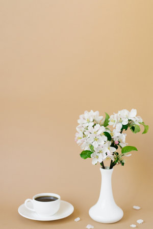 Beautiful white apple tree flowers in a white vase and a cup of tea on a beige background with a copy spaceの写真素材