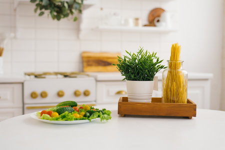Plate of vegetables, a jar of pasta and a green plant on the kitchen tableの写真素材