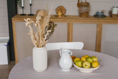 Dried flowers in a white ceramic vase, a jug of milk and apples on a tray or plate in a Scandinavian wooden kitchenの写真素材