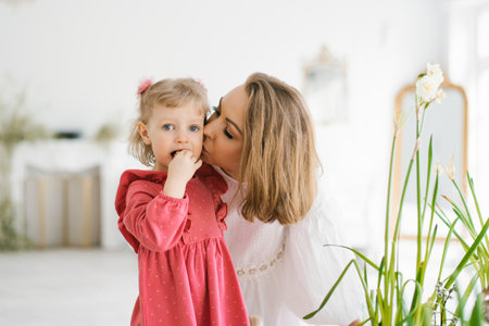 Mom kisses her three-year-old daughter on the cheek at homeの写真素材