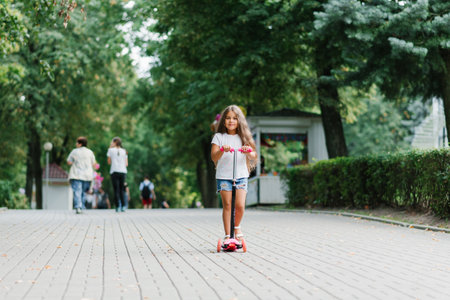 Active little child girl riding scooter on road in park outdoors on summer dayの写真素材