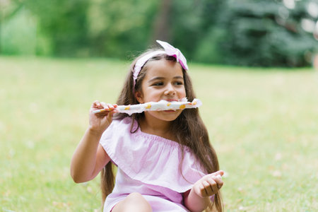 Cute baby girl in pink dress eats white cotton candy in the park in summerの写真素材