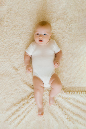 Five-month-old baby is lying on a light blanket in the bedroom. Top view of a charming boy
