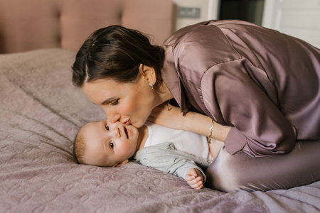 Mother kisses her baby on the bed