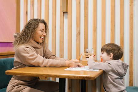 Young Caucasian mother is sitting at a table in a cafe with her four-year-old son waiting for her order and having fun communicating with each otherの写真素材