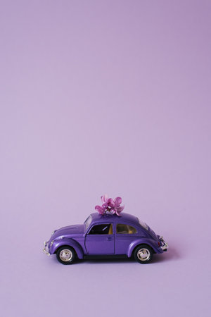 Purple toy car with lilac flowers on the roof on a lilac background. flower delivery. Birthday holiday concept, Mother's day, Valentine's day, Spring dayのeditorial素材