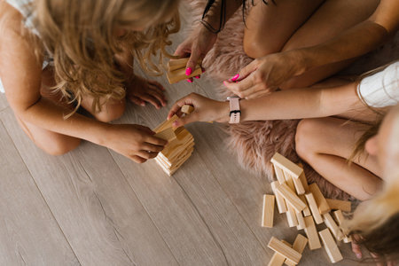 Children with their mother play building a tower of wooden cubes, sitting on the floor in the living room. Close-up of the arm and the towerの写真素材